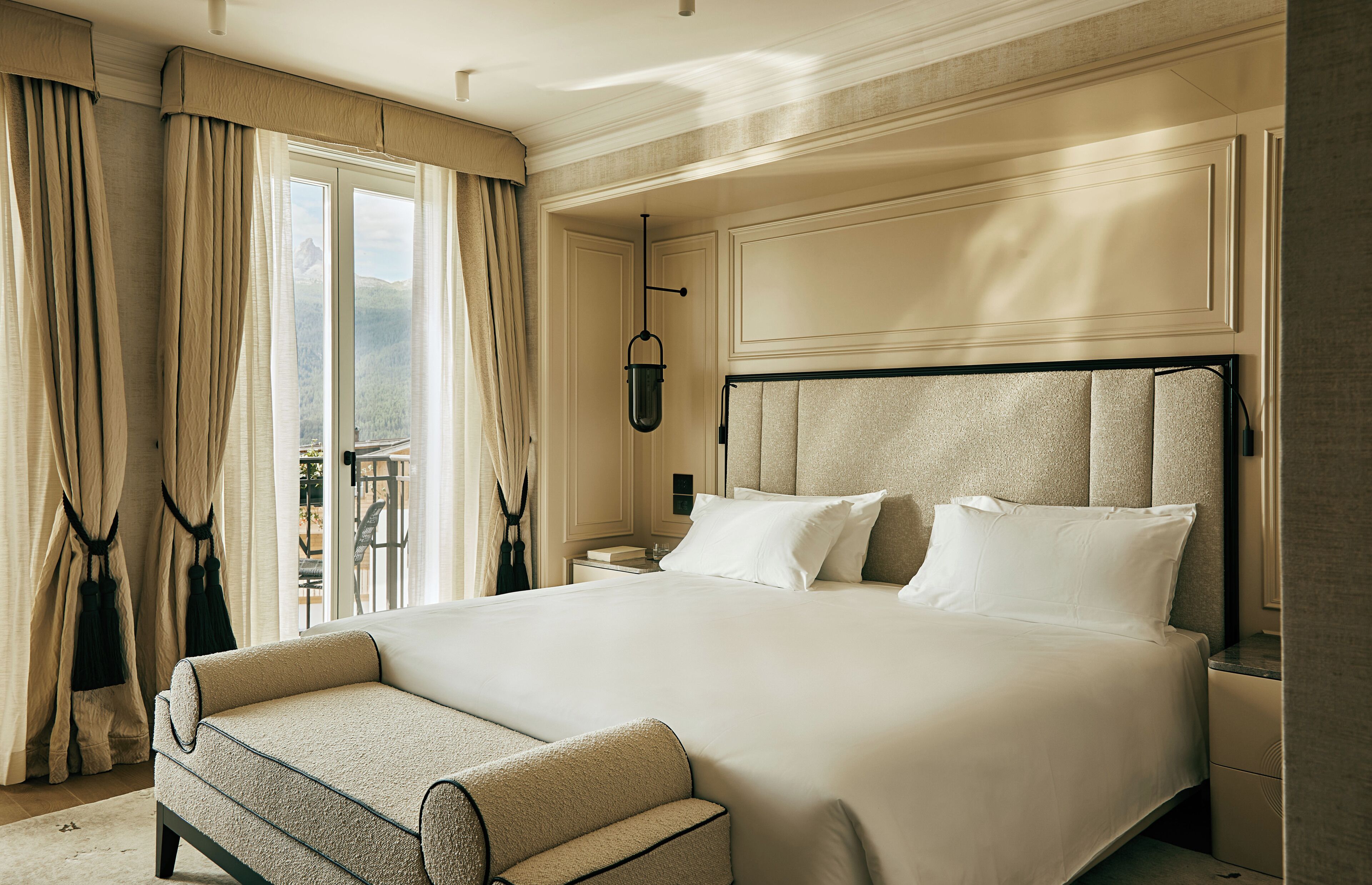Une chambre d’hôtel avec un grand lit, une table de chevet, une chaise et une vue sur un paysage montagneux par la fenêtre.