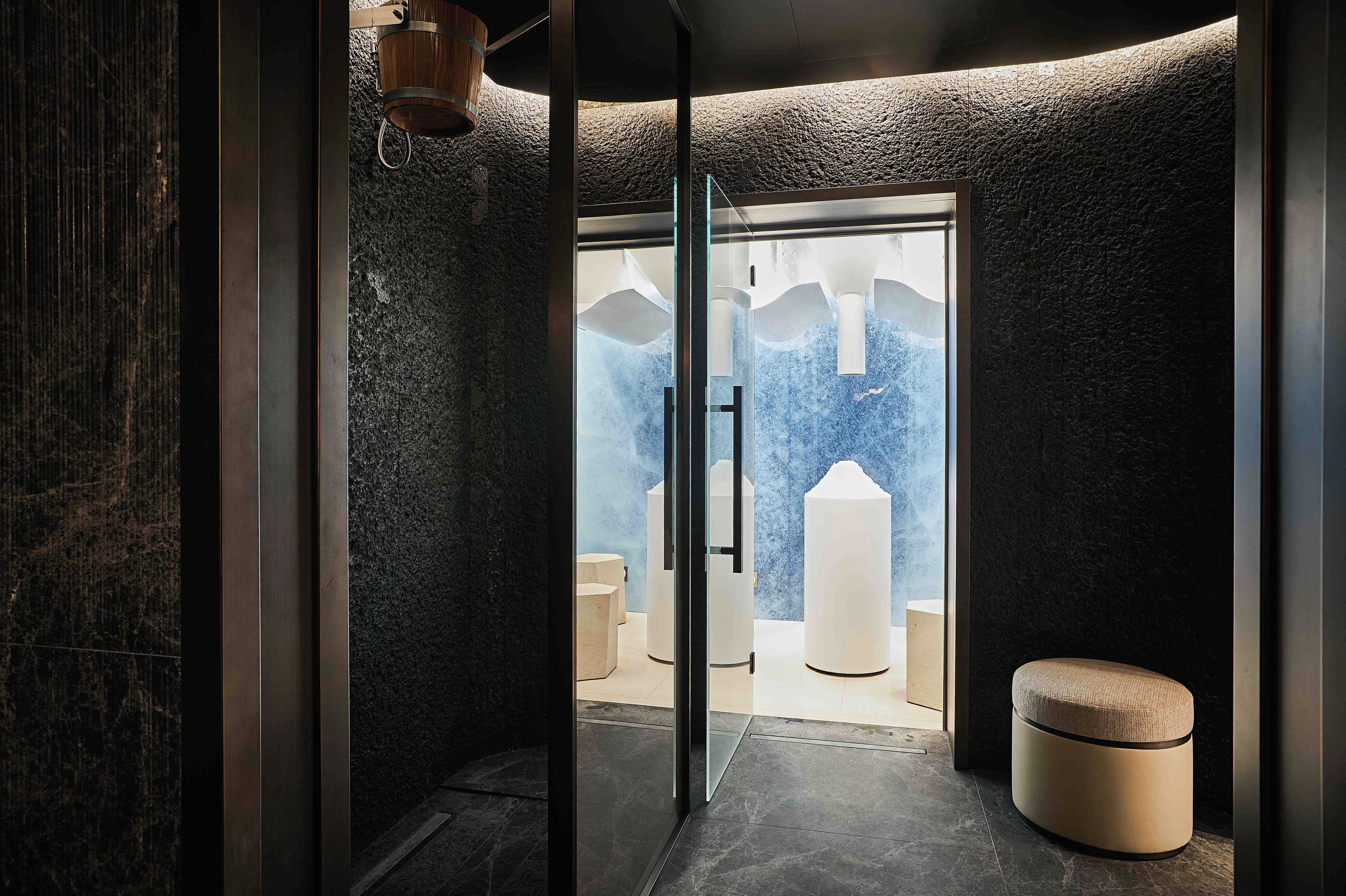 Un bagno moderno con parete in pietra, porta in vetro che dà accesso alla zona doccia e una panca rotonda.