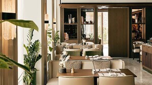 Un interior moderno con zonas de estar, una mesa de comedor para dos personas y vistas al exterior.