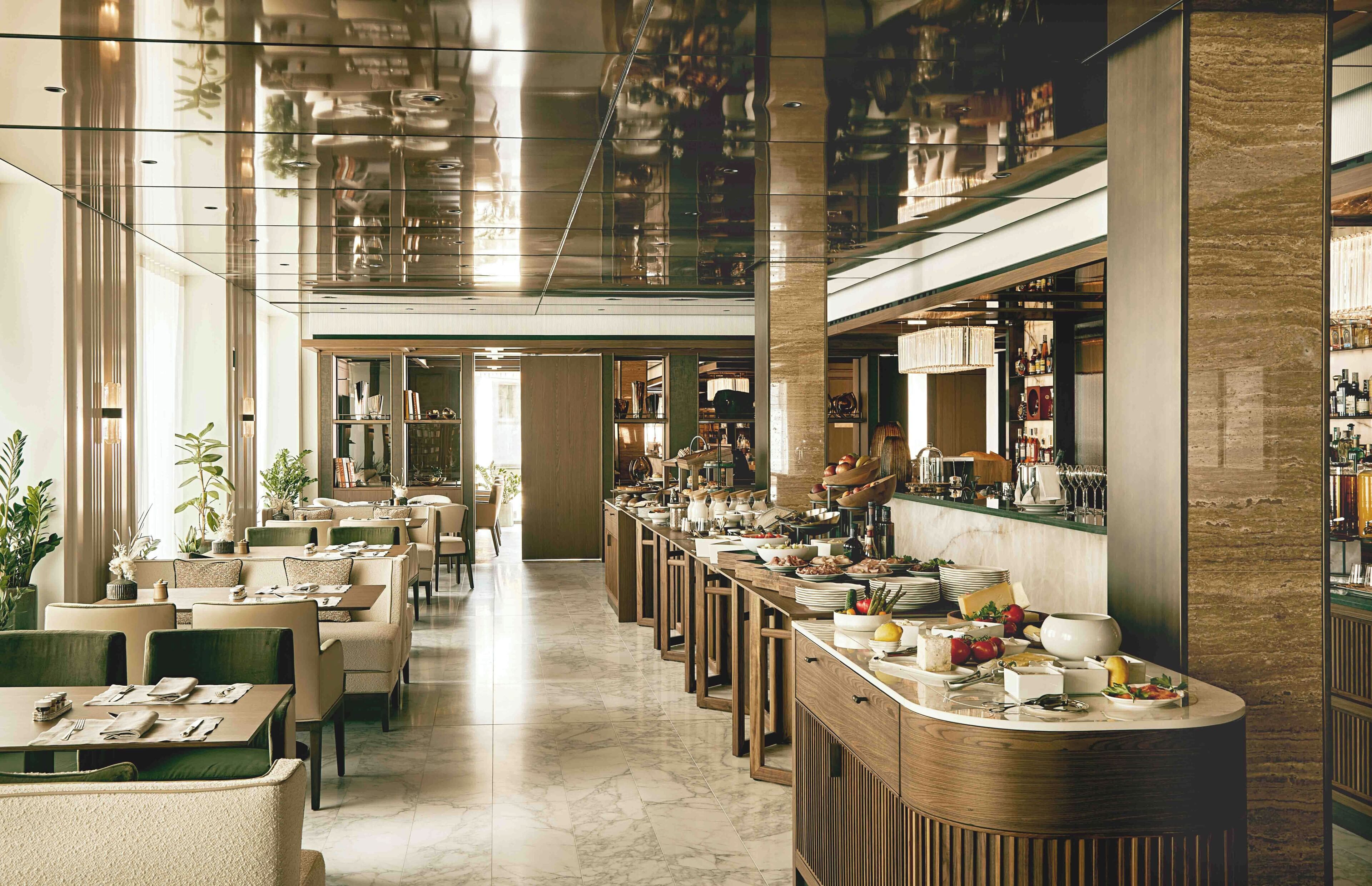 A spacious hotel lobby with a long reception desk, seating area, and a view of the bar area.