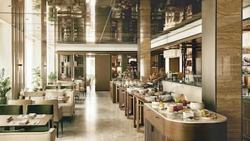 A spacious hotel lobby with a long reception desk, seating area, and a view of the bar area.