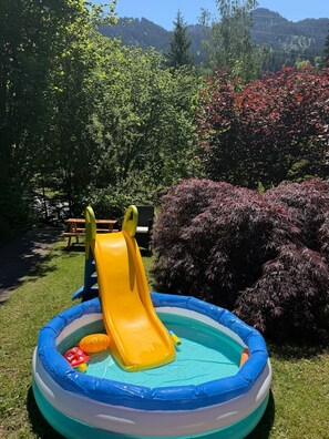 Une piscine gonflable avec un toboggan, entourée d’herbe et d’arbres.