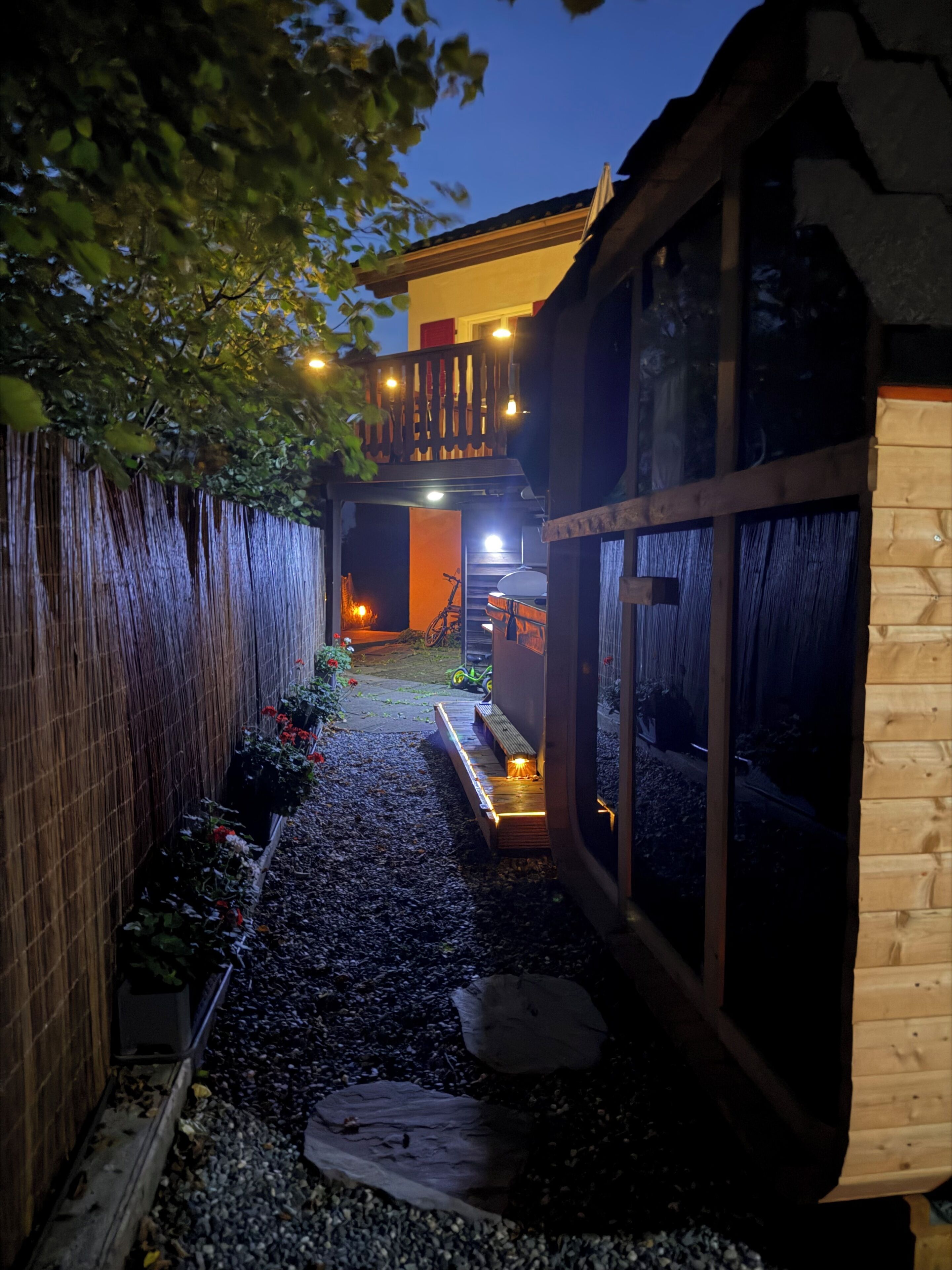 A narrow pathway leading to a wooden structure with a balcony and a staircase.