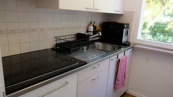 Een keuken met witte kasten, een zwart aanrecht en een raam met uitzicht op groen.