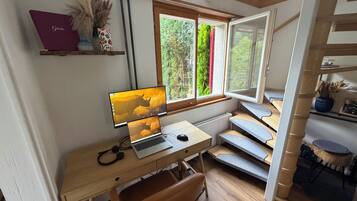 A room with a desk, computer, and a window with a view of greenery.