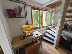 A room with a desk, computer, and a window with a view of greenery.