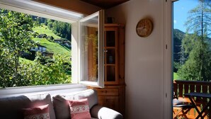 A cozy room with a sofa, a wooden cabinet, and a large window offering a view of a green landscape. - Private Chalet | Lake & Mountain Views | Sauna & Hot Tub | Large Garden (Quarten)