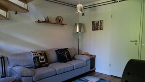 Una sala de estar moderna con un sofá gris, almohadones decorativos, una lámpara de pie y un pequeño estante de madera con objetos.