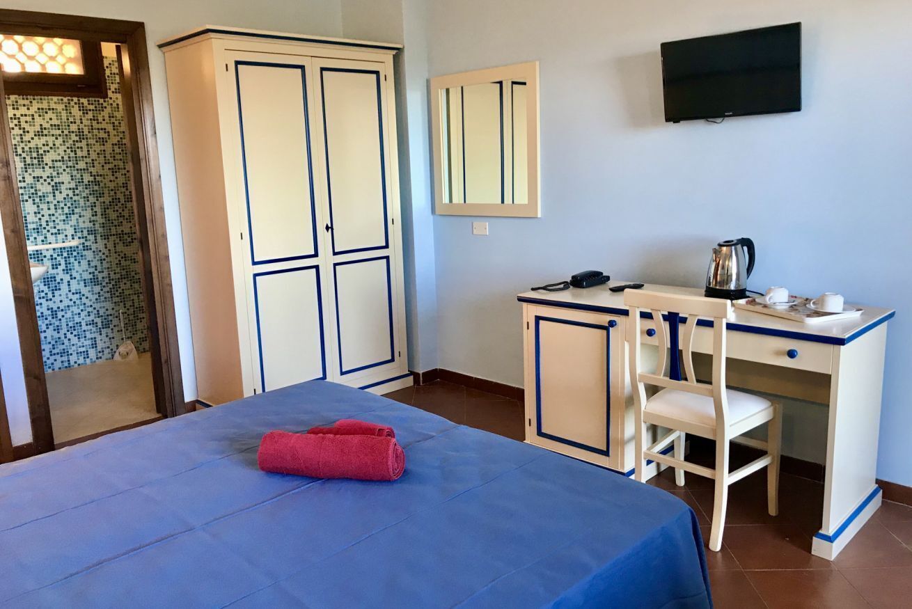 A bedroom with a bed, a desk with a chair, a television, and a wardrobe.
