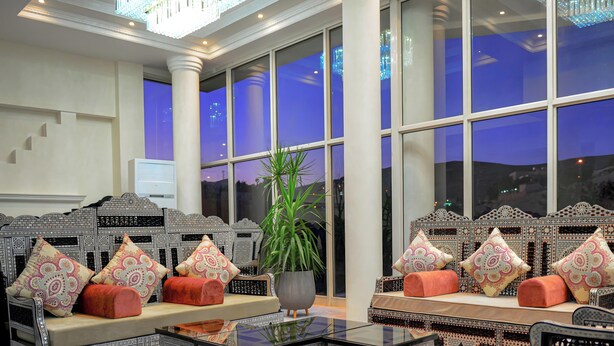 A lobby with a large window, a sofa set with patterned cushions, a potted plant, and a decorative wall. - Petra Castle Hotel (Wadi Musa)