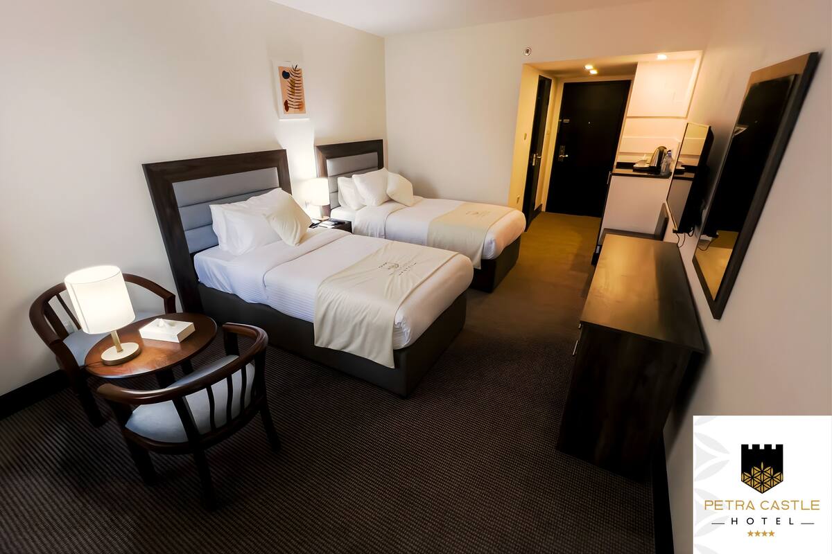 Une chambre d’hôtel avec deux lits, un bureau, une chaise et une petite table avec une lampe.