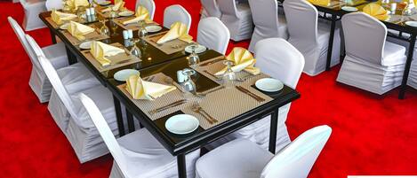 A banquet hall with tables set for a formal event, featuring white chairs and gold napkins.