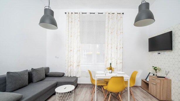 A modern living room with a grey sofa, a dining table with yellow chairs, and a TV mounted on the wall. - Łódź Legionów Apartment M1 - Parking, Top Location (Łódź)