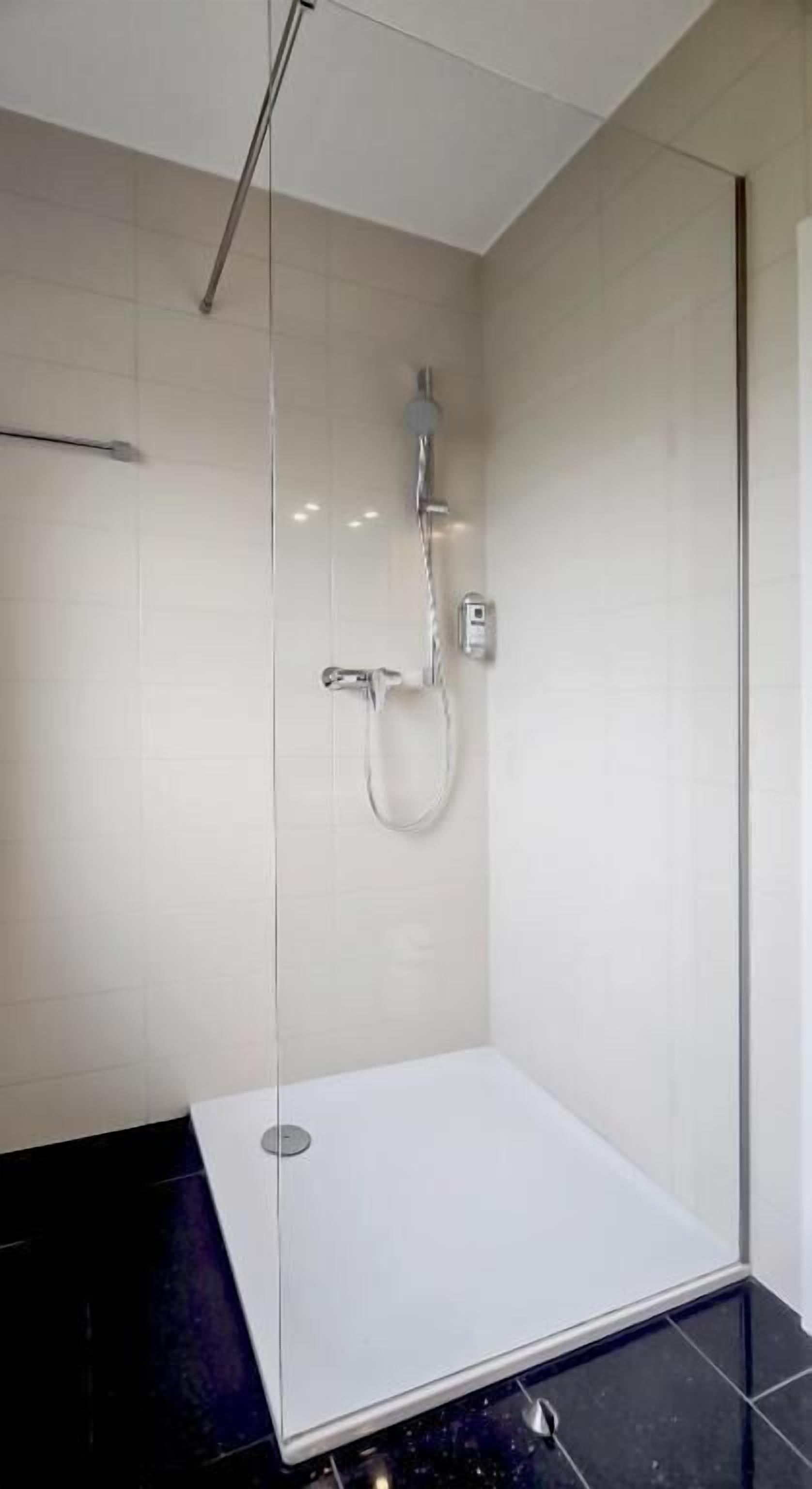 Une cabine de douche moderne dotée d’une porte en verre, d’un pommeau de douche à main et d’un robinet mural.