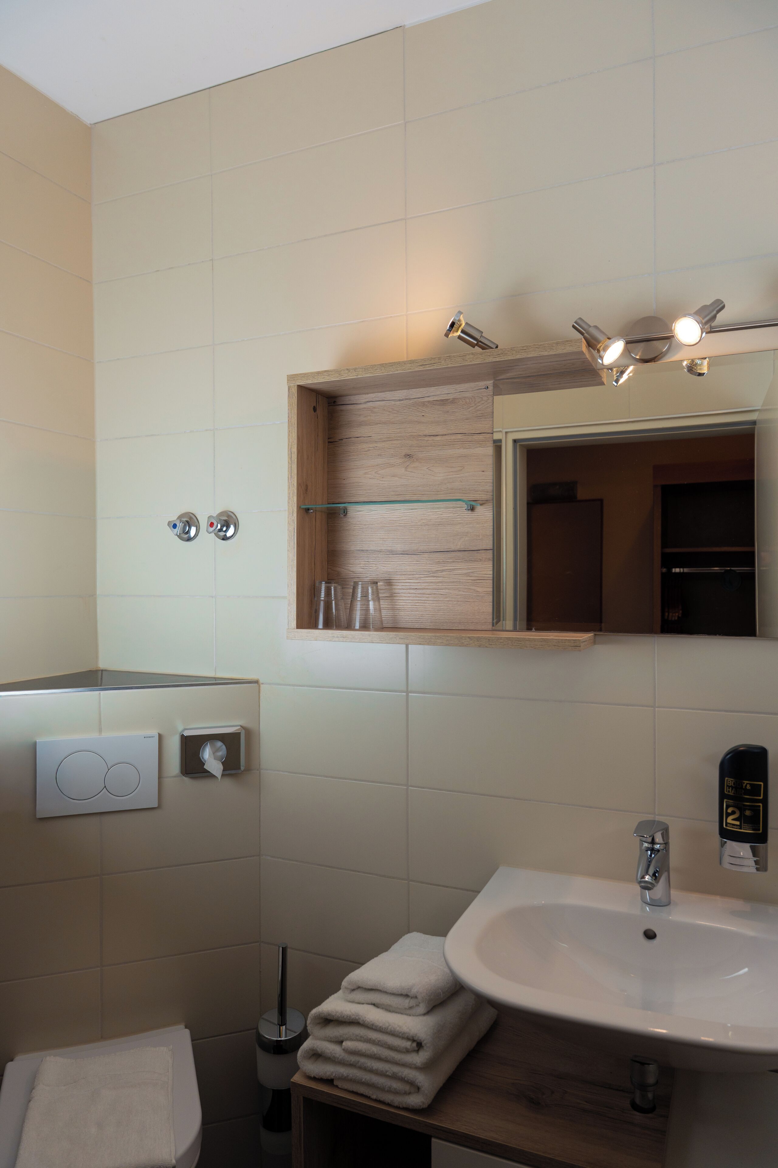 A modern bathroom with a white sink, a mirror with lights, a towel rack, and a toilet.