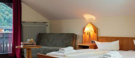 Habitación de hotel con una cama, una silla, una mesita con provisiones para el desayuno, una mesita de noche con una lámpara y vistas a zonas verdes.
