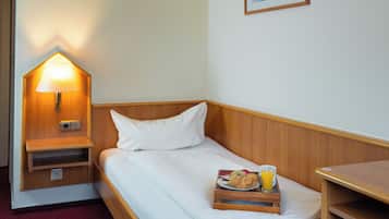 Una cama individual con cabecera de madera, una mesita de noche con lámpara, una bandeja con comida y bebida, y un cuadro en la pared.