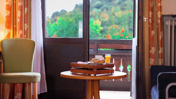 A room with a view of greenery, a dining table with breakfast items, and two chairs. - ALEMBRA - Hotel zur Moselbrücke (Schweich)