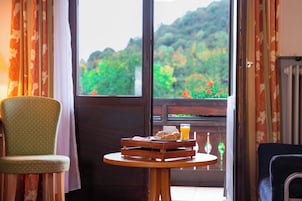 A room with a view of greenery, a dining table with breakfast items, and two chairs.