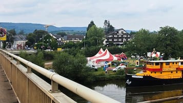 A river with a boat docked on the right, a bridge in the foreground, and a building with a sign that reads "HOTEL" in the background.