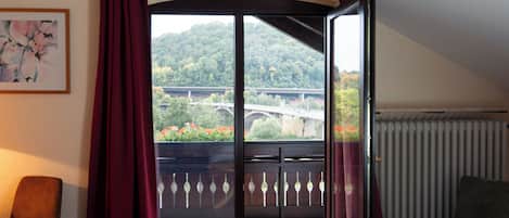 A room with a large sliding glass door leading to a balcony with a view of a bridge and greenery.