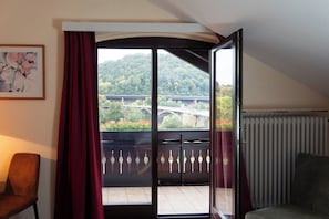 Una habitación con un amplio ventanal corredera que da a un balcón con vistas a un puente y vegetación.