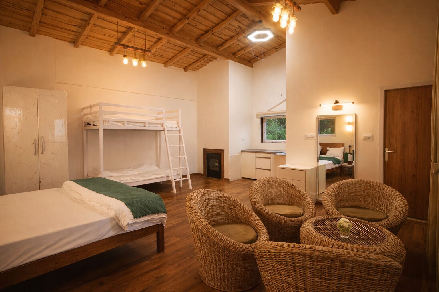 A room with bunk beds, a desk, wicker chairs, and a wooden ceiling.