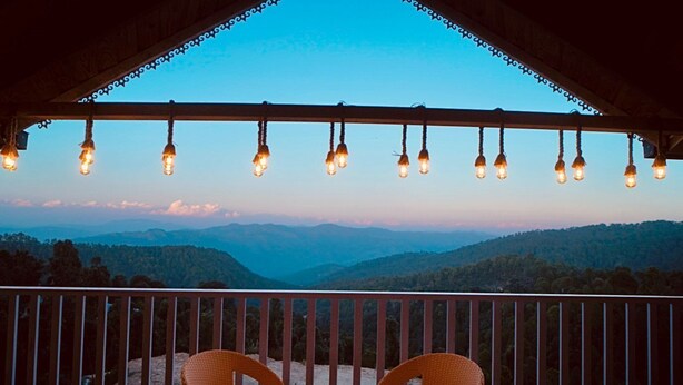 Un balcon agrémenté de chaises en osier et illuminé de guirlandes lumineuses, offrant une vue sur un paysage montagneux.