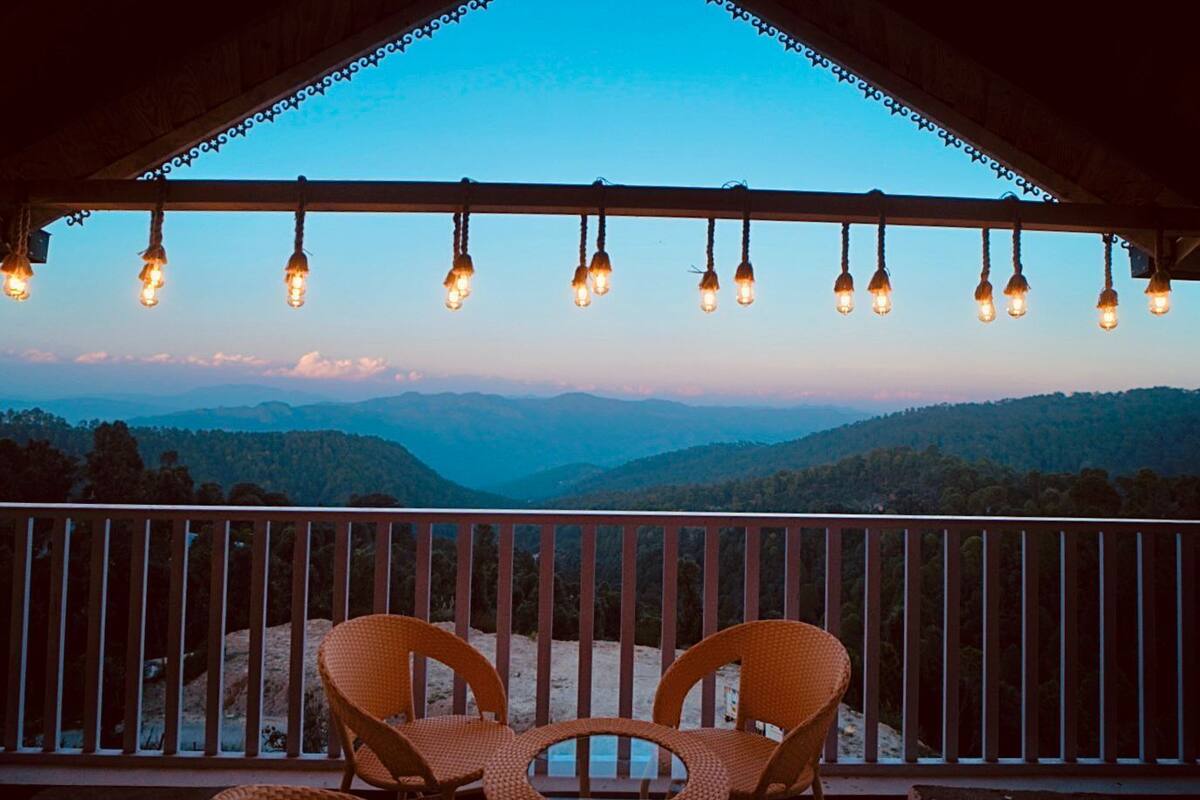 A balcony with wicker chairs and string lights, overlooking a mountainous landscape.