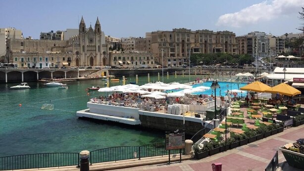 A waterfront area with a historic building, a dock with boats, and outdoor seating with umbrellas. - Seaview 1-bedroom apartment with AC in St. Julian's (St. Julian's)
