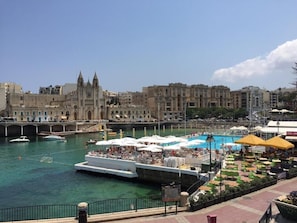 A waterfront area with a historic building, a dock with boats, and outdoor seating with umbrellas. - Seaview 1-bedroom apartment with AC in St. Julian's (St. Julian's)