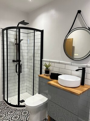 A modern bathroom with a glass-enclosed shower, a white sink with a black faucet, and a round mirror. - Apple Tree Cottage Durham (Durham)