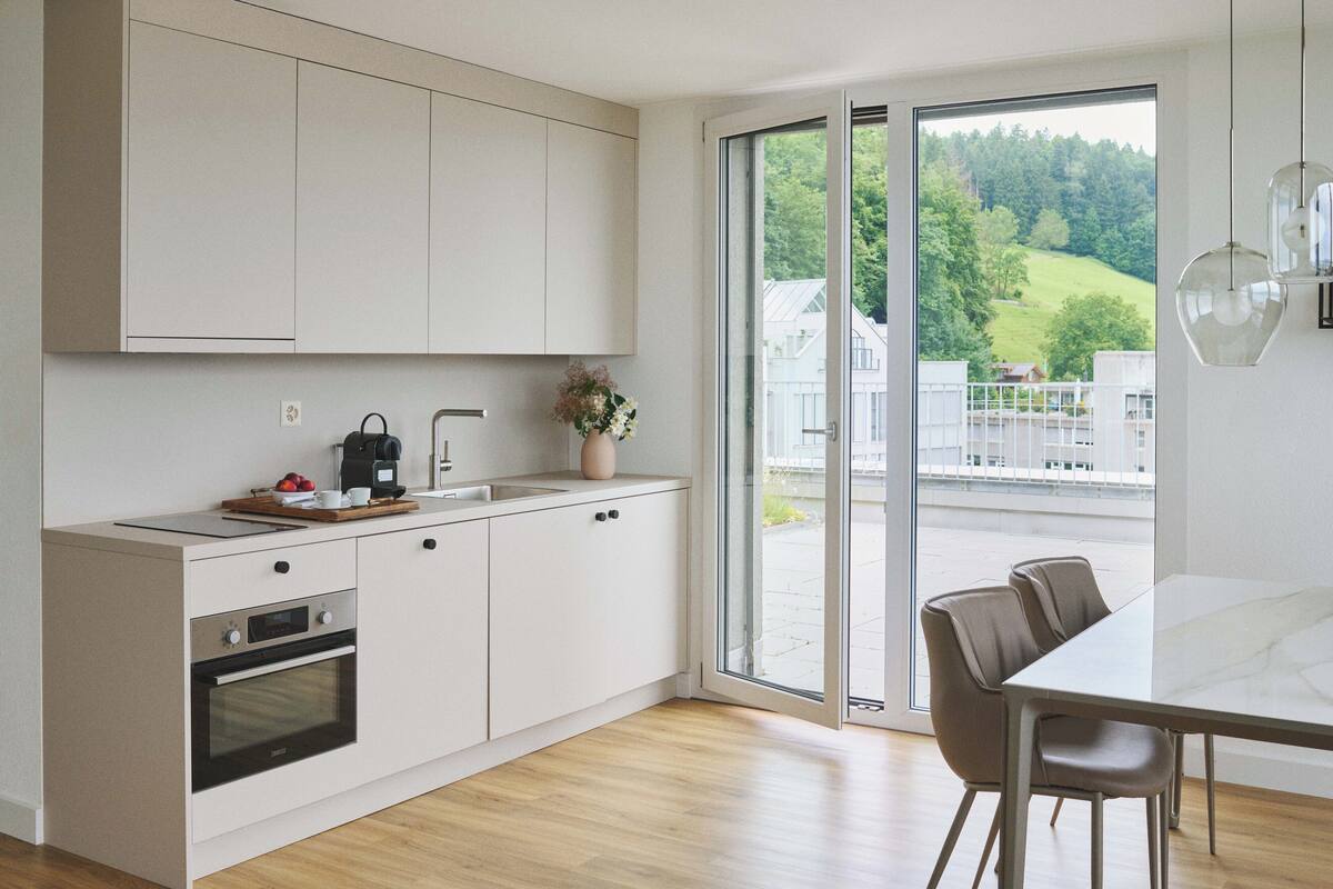 Una cocina moderna con horno integrado, cafetera y un florero con flores.