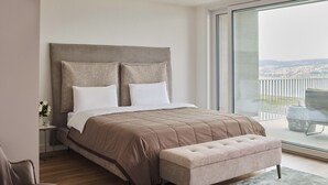 Un dormitorio moderno con una cama grande, un banco, una mesita de noche y vistas al exterior.