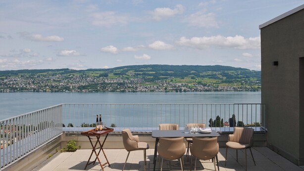 Terraza con mesa y sillas con vistas a un lago y pueblo.