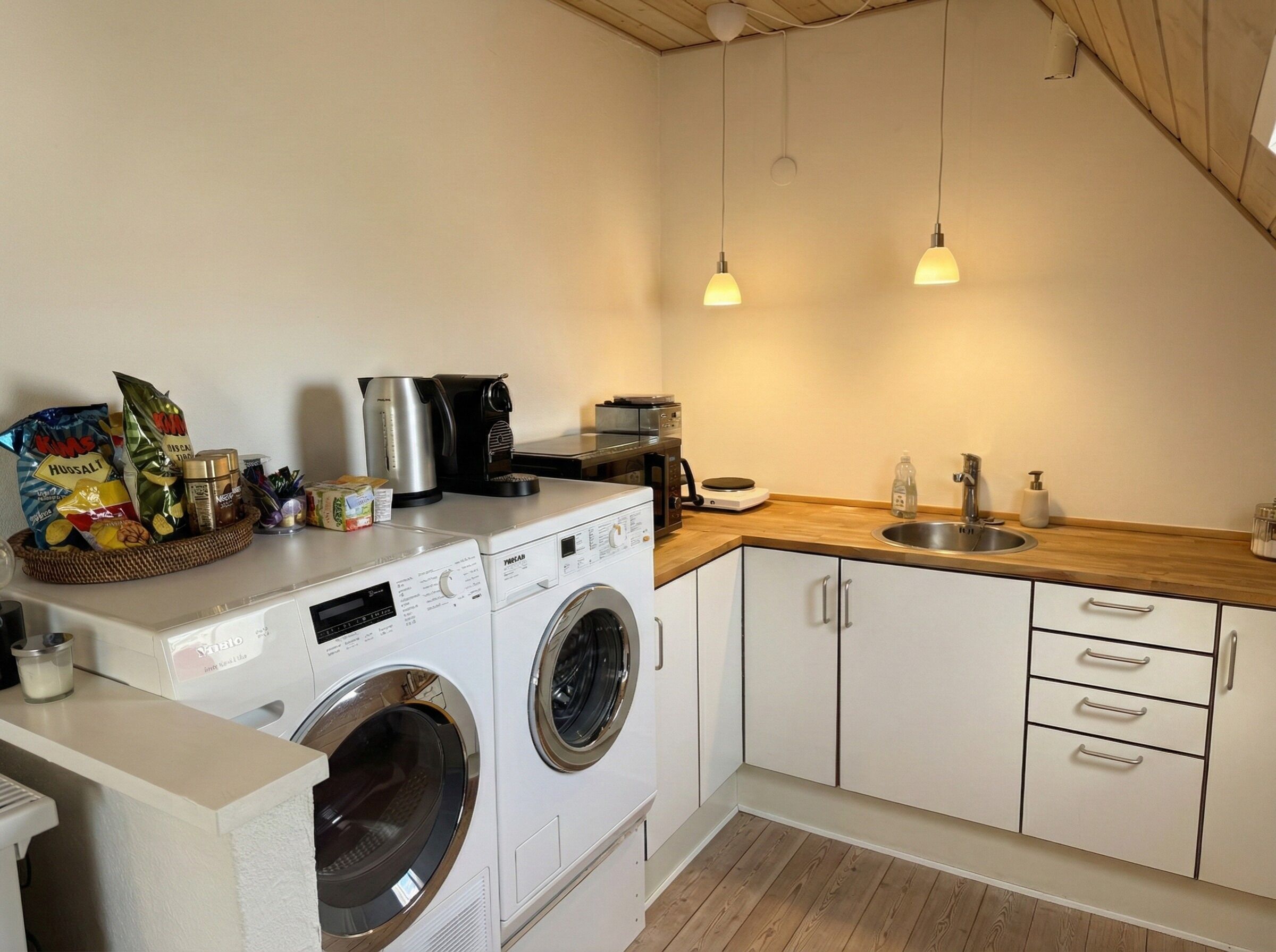 Een kleine keuken met een wasmachine, een koffiezetapparaat en een spoelbak.