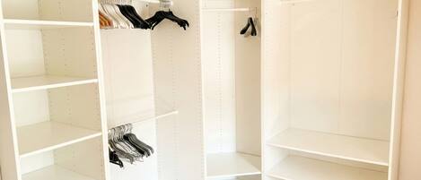 A corner closet with multiple shelves and hanging space, featuring a white interior and wooden flooring.
