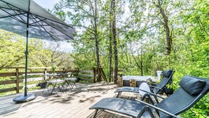 A wooden deck with outdoor furniture, including lounge chairs and a table, surrounded by trees. - Premium Dome & hot tub – Nature in Dordogne (La Dornac)