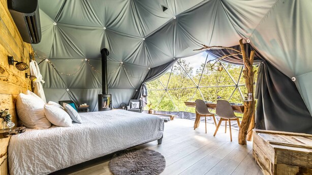 A cozy tented accommodation with a bed, a small table, and chairs. - Premium Dome & hot tub – Nature in Dordogne (La Dornac)