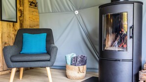 A modern living room with a black wood-burning stove, a grey armchair with a blue cushion, and a woven basket with blankets. - Premium Dome & hot tub – Nature in Dordogne (La Dornac)