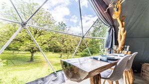 A dining area with a large table and chairs, a view of a grassy landscape through a tent-like structure, and a wooden tree trunk decoration. - Premium Dome & hot tub – Nature in Dordogne (La Dornac)