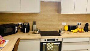 A kitchen with a microwave, toaster, kettle, and a small oven. There are fruits and a coffee maker on the counter. - Corby- Split Level Apartment With 3 Bedrooms (Corby)