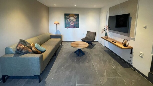A modern living room with a sofa, two chairs, a coffee table, a TV, and a painting on the wall. - Spacious Holliday home in authentic farmhouse with terrace view (Voerendaal)
