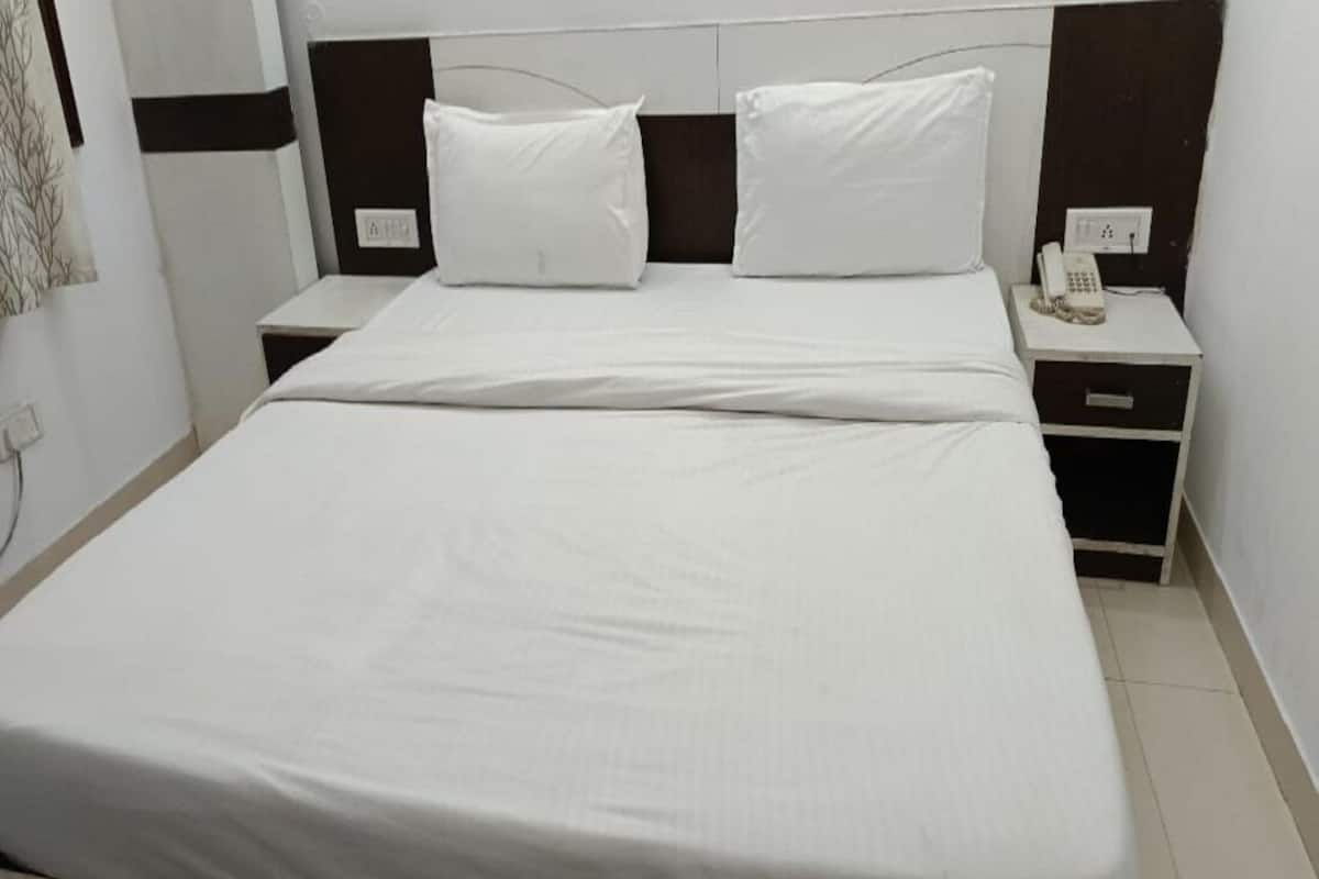 A neatly made bed with white linens, a bedside table with a telephone, and a nightstand with a lamp.