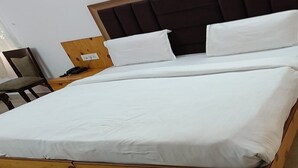 A bed with white linens, a wooden headboard, and a nightstand with a lamp. - Hotel TJS Grand (New Delhi)