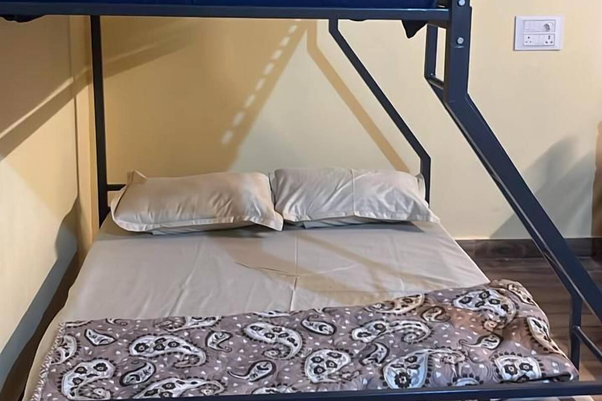 Ein Stockbett mit gemustertem Topper und Kissen, eine Steckdose und ein Lichtschalter.