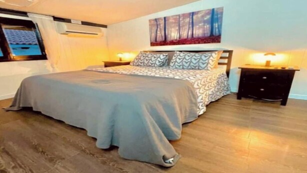 Een slaapkamer met een bed, een nachtkastje, een schilderij aan de muur en een raam.