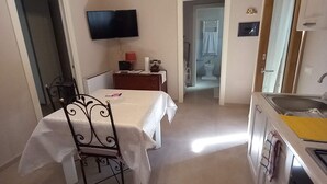 Ein Zimmer mit Bett, Tisch mit Stuhl, Fernseher, Badezimmer mit Dusche und Küchenzeile.