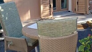 Ein Sitzbereich im Freien mit Korbstühlen und einem Tisch, eine Schiebeglastür und ein kleiner Garten mit Pflanzen.