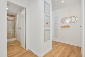 A hallway with a wooden floor, white walls, and framed artwork.